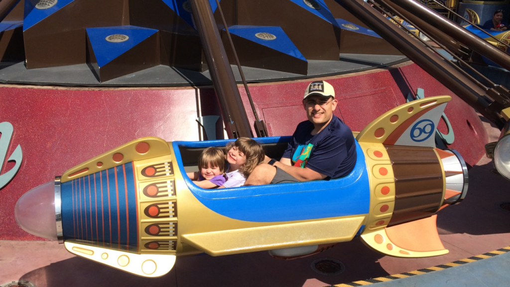 Man and two children ride colorful theme park rocket
