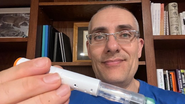 Man holding a syringe-like medical device near camera
